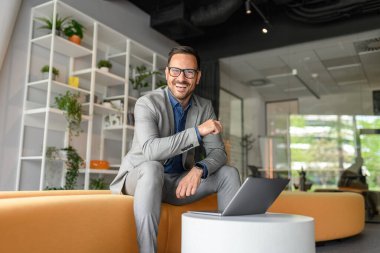 Koltukta oturup bilgisayarın başında çalışan neşeli genç işadamının düşük açılı portresi.