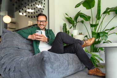 Ofisteki koltukta akıllı telefondan sosyal medya pazarlaması yapan ilham verici iş adamının düşük açılı görüntüsü