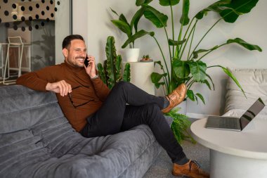 Ofisteki koltukta otururken cep telefonuyla konuşan neşeli iş adamı.