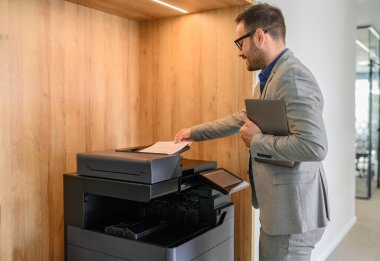 Modern ofiste erkek profesyonel dizüstü bilgisayar ve fotokopi makinesine kağıt koyarken yan görünüm