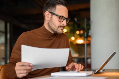 Gözlüklü kendine güvenen işadamının portresi ofiste dizüstü bilgisayarla araştırma yapıyor.