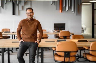 Kendine güvenen profesyonel bir erkeğin portresi. Elleri ceplerinde. Salondaki tahta masada oturuyor.