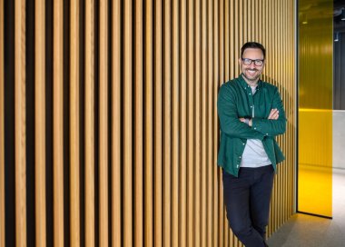 Kollarını kavuşturup kameraya gülümseyen ve ofiste tahta duvarda poz veren kendine güvenen erkek CEO portresi.