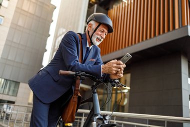 Modern şehirde bisiklete yaslanırken cep telefonu kullanan sakallı yaşlı işadamının düşük açılı görüntüsü