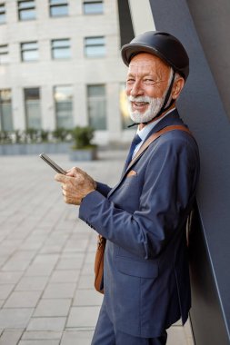 Bisiklet kaskı takmış, sokakta dururken akıllı telefon kullanan yaşlı bir profesyonelin portresi