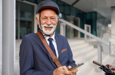 Kasklı, kendinden emin, akıllı telefondan mesaj atan ve kameraya gülümseyen profesyonel bir erkek portresi.