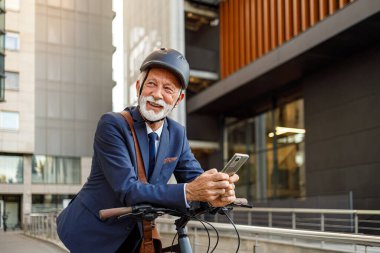 Mutlu erkek girişimci işe giderken cep telefonuyla mesajlaşıyor ve bisiklete yaslanıyor.