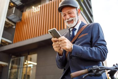 Miğferli, neşeli, yaşlı bir adamın cep telefonuyla mesajlaşırken şehir içi seyahatinin düşük açılı görüntüsü.