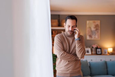 Ciddi bir orta yaşlı adamın portresi akıllı telefondan tartışırken evde beyaz perdenin önünde duruyor.