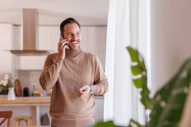 Mutlu yakışıklı bir adamın portresi telefon görüşmesi yapıyor ve evinin penceresinde dikiliyor.