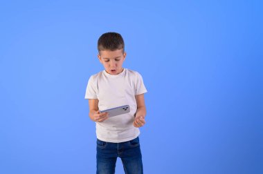 Akıllı telefondan video oyunu oynayan ve mavi arka planda yumruğunu sallayan çocuğun portresi