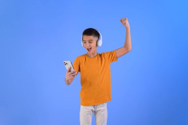 Heyecanlı çocuğun portresi, mavi arka plandaki akıllı telefondan çığlıklar atarak yükseliyor.