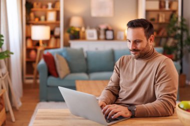 Oturma odasında masa başında çalışırken internetten araştırma yapan yakışıklı bir serbest yazar.