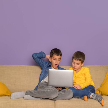 Kanepede mor arka planda otururken kardeşiyle film izleyen şaşkın çocuk.