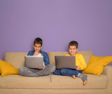 Gülümseyen kardeşlerim film izleyip bilgisayar başında mor arka planda dizüstü bilgisayar oynuyorlar.