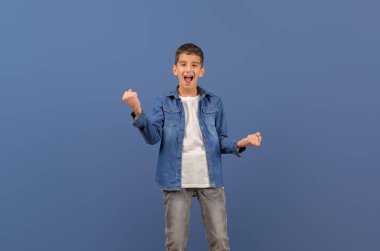 Başarılı genç iş adamının portresi mavi arka planda çığlık atıyor ve yumruklarını sallıyor.