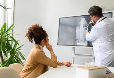 Omurga röntgenini hastanede kadın hastaya gösteren ve açıklayan erkek doktor.