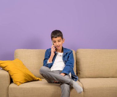 Genç girişimci, mor arka planda koltukta otururken cep telefonundan konuşuyor.