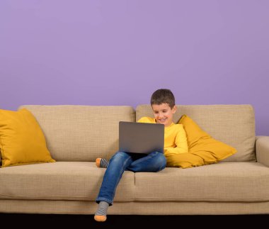 Mutlu şirin iş adamı, mor arka planda koltukta dinlenirken dizüstü bilgisayarla çalışıyor.