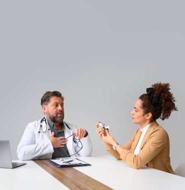 Erkek doktor göğsüne dokunuyor ve klinikteki masada otururken solunum cihazını kadınlara nasıl kullanacağını anlatıyor.