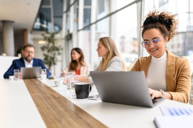 Profesyonel toplantı sırasında arka planda iş birliği yapan hukukçu meslektaşlarıyla bilgisayarındaki gülen avukat raporunu inceliyor.