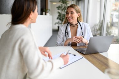 Laboratuvar önlüklü gülümseyen doktor muayene sırasında hastanın semptomlarını açıklamasını dinliyor.