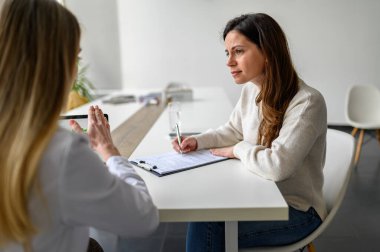 Kadın form dolduruyor ve tıbbi danışmanlık sırasında semptomları ve tedaviyi açıklayan doktoru dinliyor.