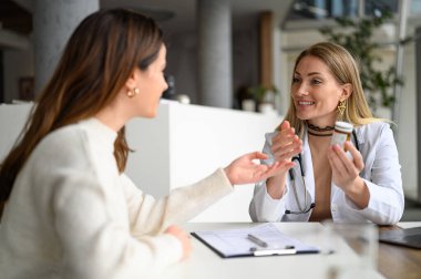 Elinde ilaç şişesi olan kadın doktor, hastanede muayene sırasında hastaya dozajı ve talimatları açıklıyor.