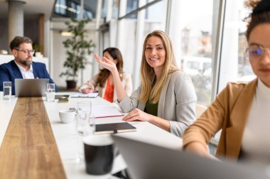Masasında not defteri olan kendine güvenen bir iş kadını modern ofisteki profesyonel ekiple işbirliği yapıyor.