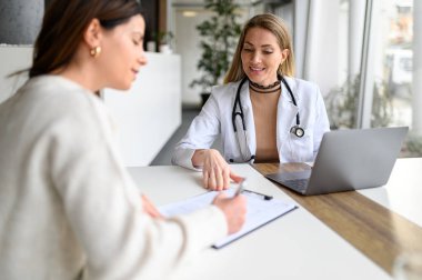 Laboratuar önlüklü kadın doktor, hastalar hastanedeki panoya detayları yazarken dizüstü bilgisayarla çalışıyor.