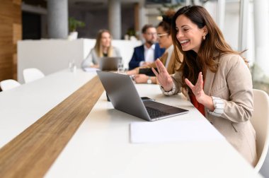 Neşeli iş kadını arka planda çalışan meslektaşlarıyla çevrimiçi toplantı sırasında iş stratejisini bilgisayarda tartışıyor.