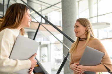 Sırıtkan kadın girişimciler ellerinde dizüstü bilgisayarlarla ofiste dururken iş stratejilerini tartışıyorlar.