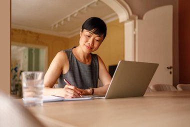 Kadın avukatın düşük açılı portresi notlar yazıyor ve şirket ofisinde dizüstü bilgisayarla çalışıyor.