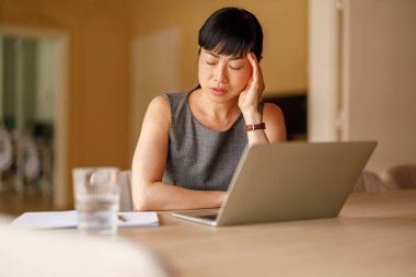 Yetişkin bir iş kadını ofis masasında dizüstü bilgisayarla çalışırken stresli ve acı içinde.