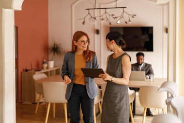 Şirket ofisinde yan yana dururken dijital tablet üzerinden çevrimiçi verileri tartışan kadın meslektaşlar