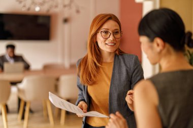 Gözlüklü kendine güvenen kadın muhasebeci modern ofisteki meslektaşımla mali raporları tartışıyor.