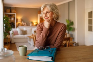 Fotoğraf albümüyle evde tek başına oturan son sınıf öğrencisi kadın. Düşünceli bir ifadeyle geçmiş anılarını hatırlıyor.