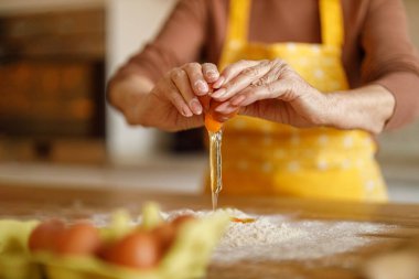 Evde blogu için şeker hazırlarken mutfak tezgahında una yumurta kıran yaşlı kadının elleri.