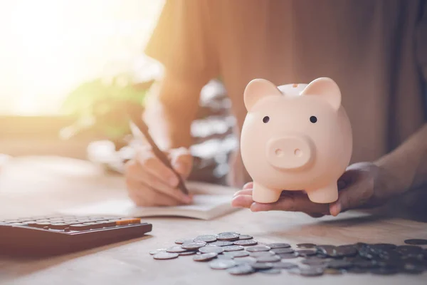 stock image Man hand holding piggy bank with calculator and coin on wood table. Saving money wealth and financial concept. Business, finance, investment, Financial planning.