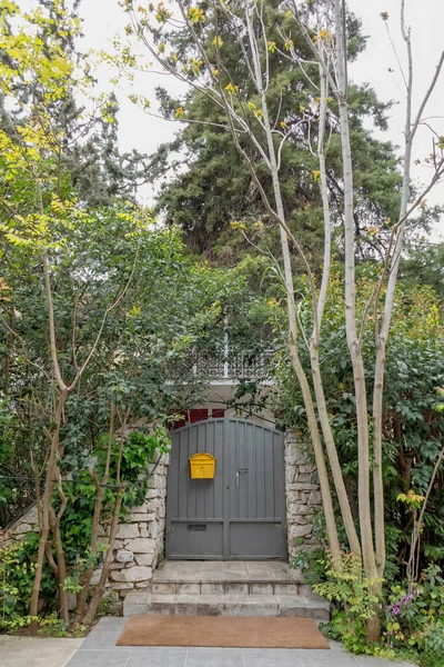 stock image trees surrounding house entrance grey door with vibrant yellow mail box, Athens Greece