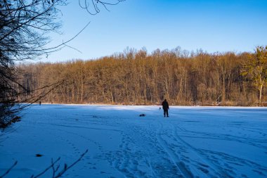 Tanımlanamayan balıkçı figürü silueti balık ısırığı, buzda balık oltası donmuş bir nehir çukurunda hazır, dace ısırığı, karda insan izleri, kış ormanı günbatımı, popüler açık hava hobisi