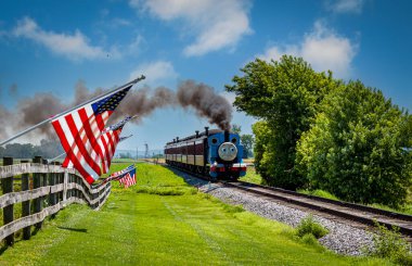 Strasburg, Pennsylvania. 48 Haziran 2021 - Güneşli bir günde Çit Üzerinde Amerikan Bayraklarını Geçerken Yolcu Arabalarını Çeken Thomas