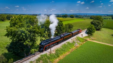 Drone View of an Antique Steam Engine, Blowing Steam and Traveling Along the Countryside Pulling a Caboose on a Sunny Day