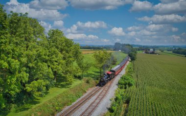 Drone View of an Antique Steam Engine, Approaching, Blowing Steam and Traveling Along the Countryside on a Sunny Day