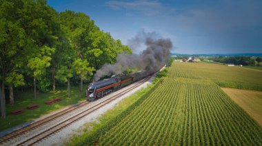 Drone View of an Antique Steam Engine, Approaching, Blowing Steam and Traveling Along the Countryside on a Sunny Day