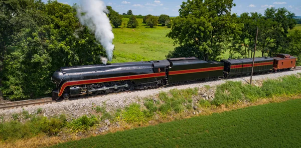 stock image Drone View of an Antique Steam Engine, Blowing Steam and Traveling Along the Countryside Pulling a Caboose on a Sunny Day