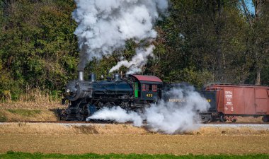 Ronks, Pennsylvania, November 8, 2021 - A View of a Restored Steam Freight Train Blowing Smoke and Steam Traveling Along a Rural Countryside on a Sunny Day