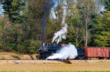 A View of a Restored Steam Freight Train Blowing Smoke and Steam Traveling Along a Rural Countryside on a Sunny Day