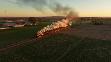 Drone View of Above and in Front of a Steam Engine Approaching Blowing Lots of Smoke at Sunrise Traveling Thru the Farmlands on Fall Morning