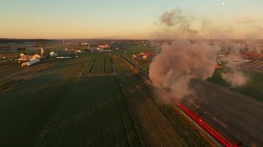 Drone View From Above and Behind of a Steam Engine Approaching Blowing Lots of Smoke at Sunrise Traveling Thru the Farmlands on Fall Morning